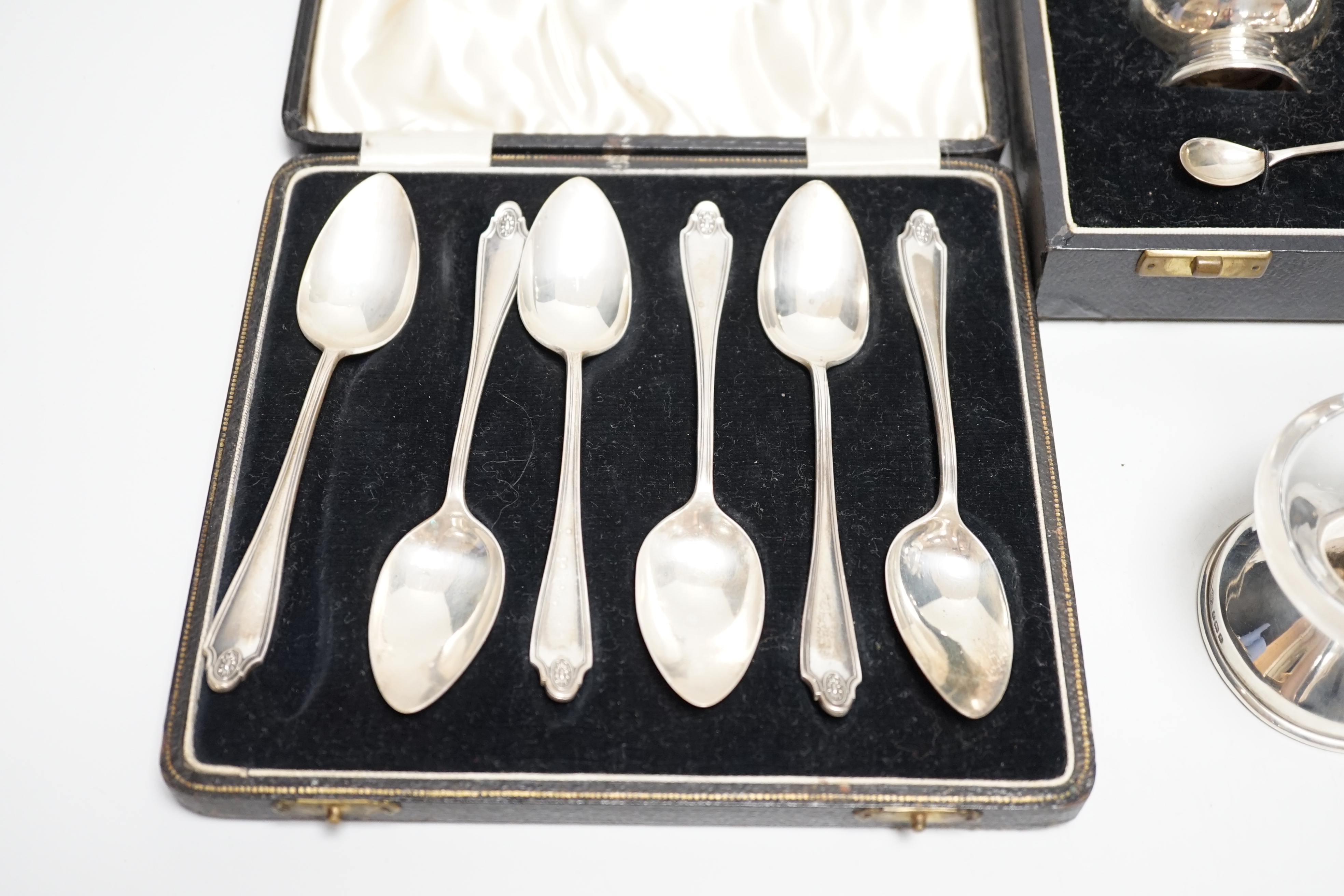 A cased George V silver three piece condiment set with two spoons, London, 1935, a cased set of six silver grapefruit spoons, a silver mounted glass pepper grinder and a white metal mounted glass match strike.
